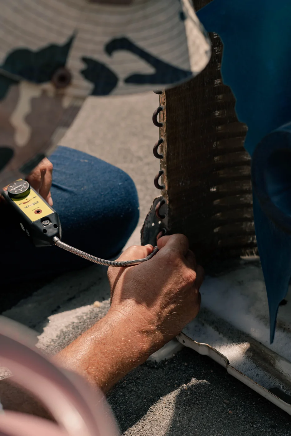 Gros plan sur les mains d’un technicien contrôlant une batterie de climatiseur avec une sonde. Photo illustrative.